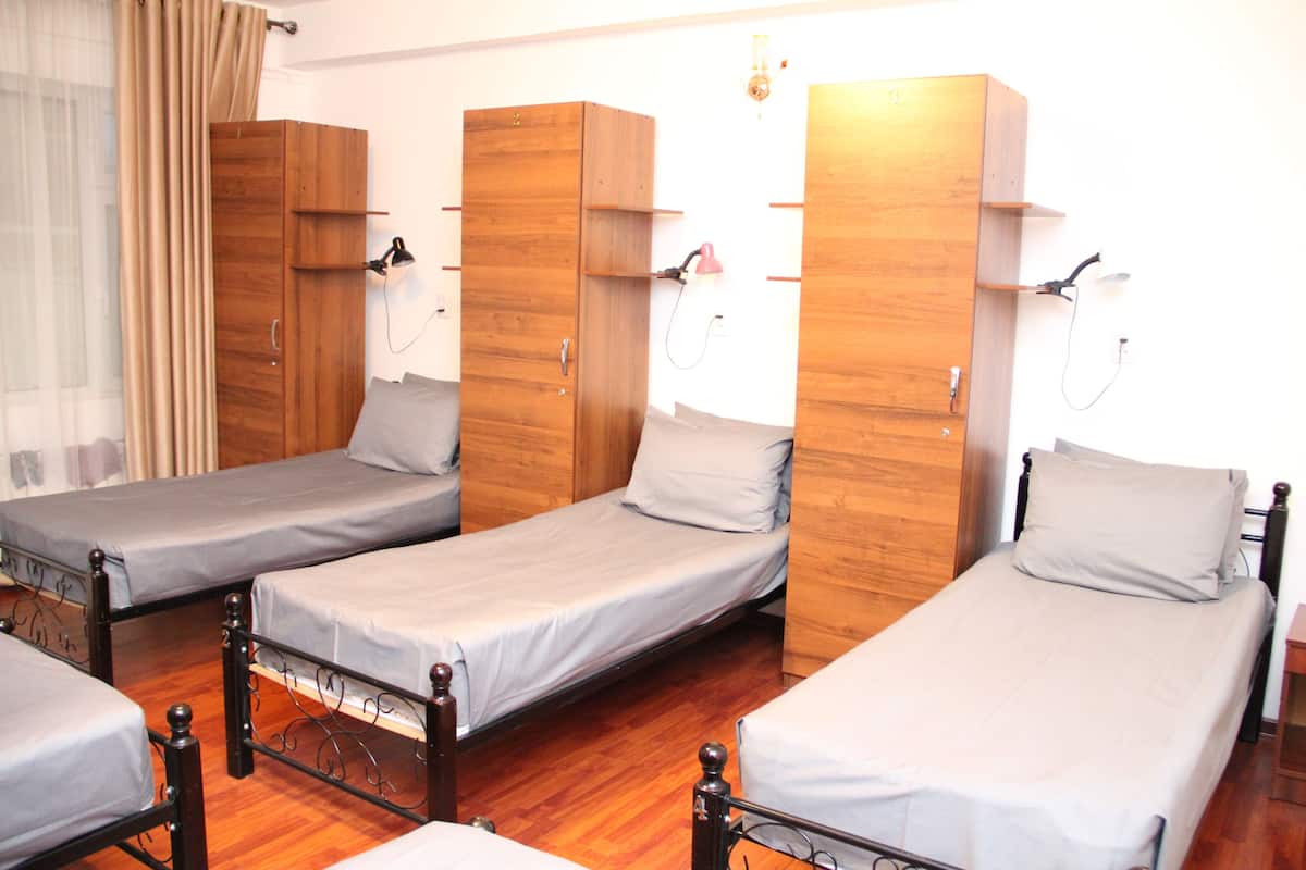 A dormitory room with four single beds, wooden wardrobes, and a window with curtains.