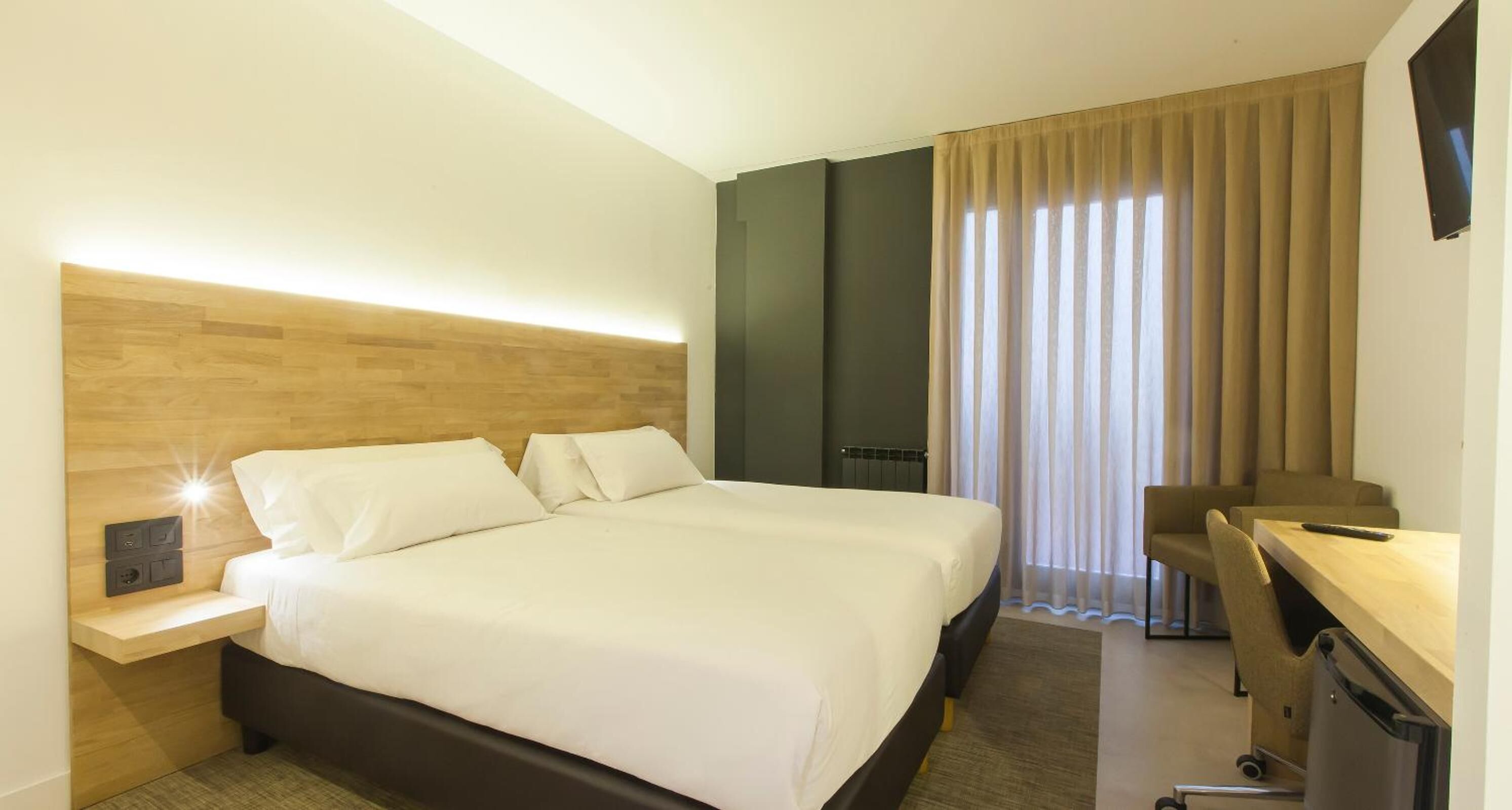 Een hotelkamer met een groot bed, een bureau, een stoel, een televisie en een raam met gordijnen.