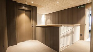 En modern hotellkorridor med träväggar, en receptionsdisk och en skylt som visar var utgången är.