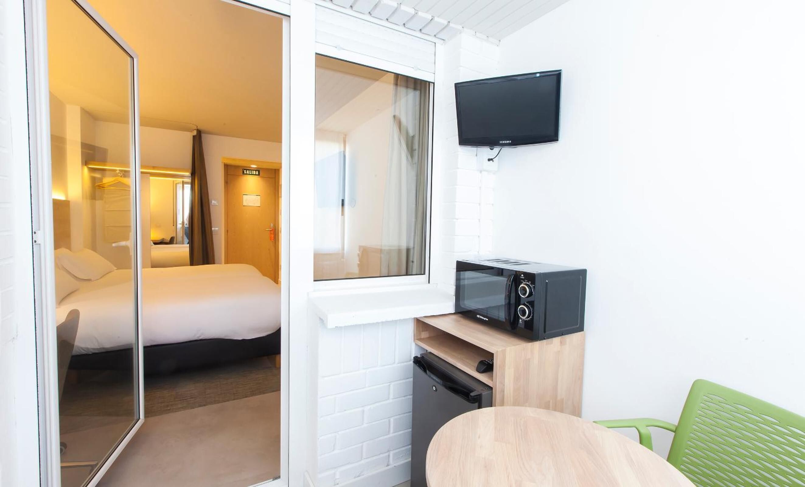 Een hotelkamer met een bed, een aan de muur bevestigde televisie, een magnetron en een kleine tafel met een stoel.