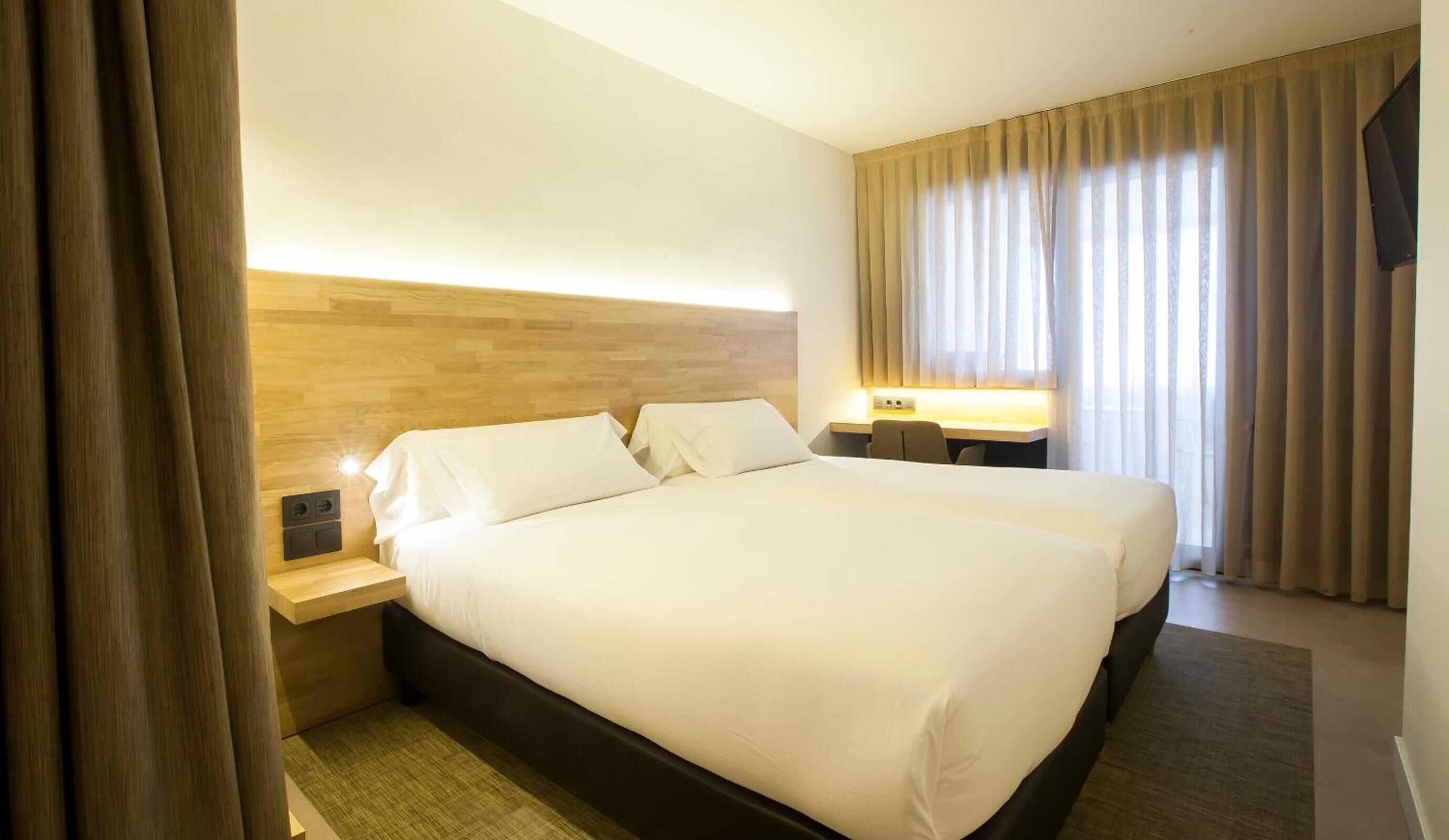 Habitación de hotel con una cama grande, dos mesitas de noche, un escritorio y una televisión.