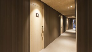 En hotellkorridor med träpanel på väggarna, ett heltäckningsmatta på golvet och en dörr med en skylt som visar var nödutgången finns.