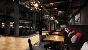 Un bar moderno con techos altos, vigas a la vista y una barra larga con taburetes.