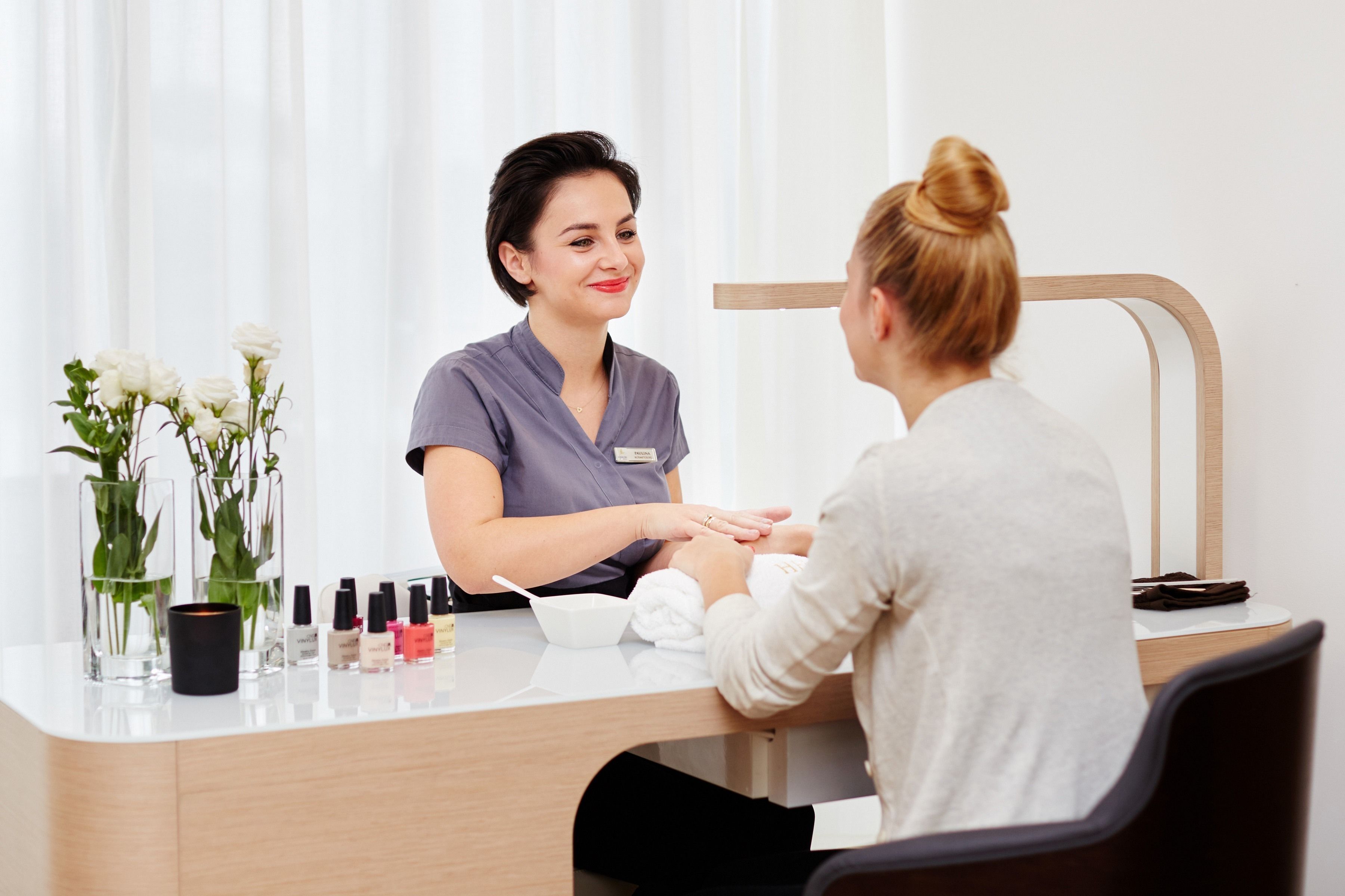 A reception desk with a vase of white flowers, a candle, and nail polish bottles.