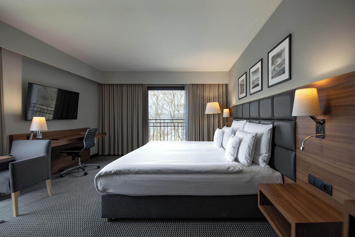 A hotel room with a large bed, a desk, a chair, a TV, and a window with curtains.