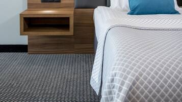 A hotel room with a bed, a nightstand, a wall-mounted lamp, and two framed pictures.