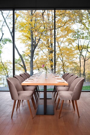 A dining table set with chairs, a vase with flowers, and a view of autumn trees through large windows. - Heron Live Hotel (Grodek Nad Dunajcem)