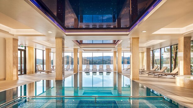 Una amplia piscina interior con agua cristalina, rodeada de tumbonas y grandes ventanales con vistas al paisaje.