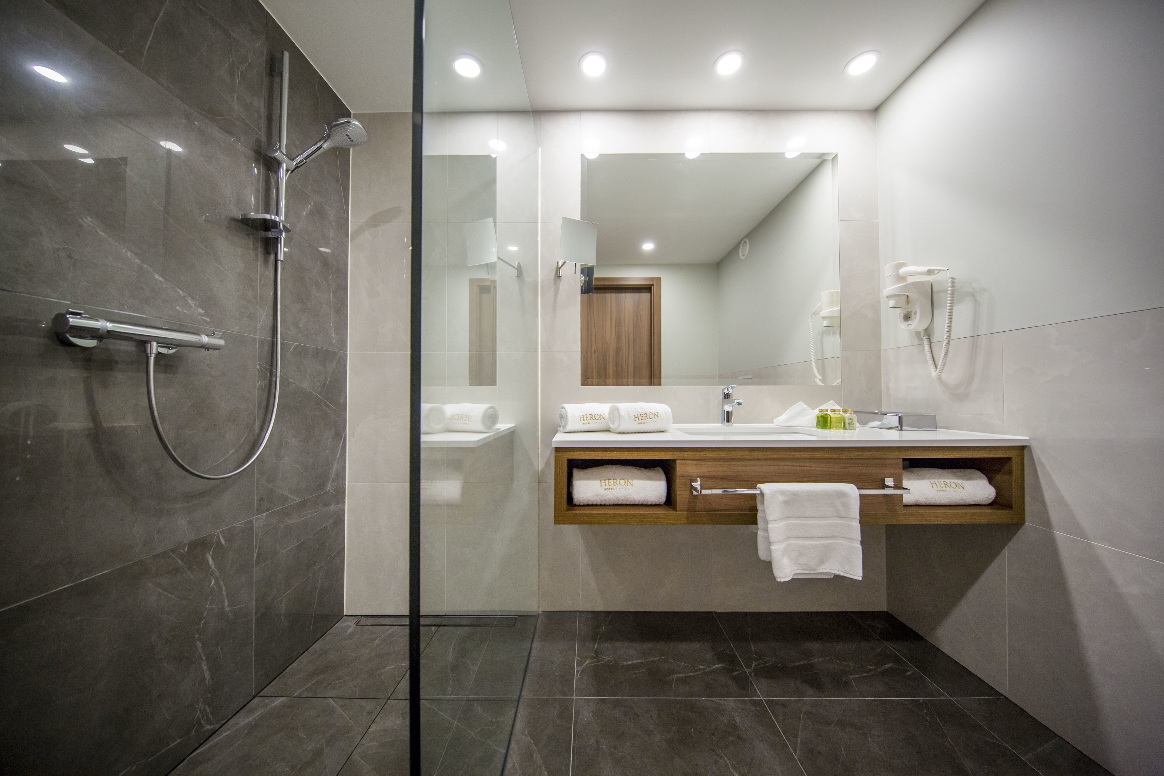 Une salle de bain moderne dotée d’une douche à parois de verre, d’un meuble-lavabo en bois avec un porte-serviettes et d’un miroir au-dessus du lavabo.