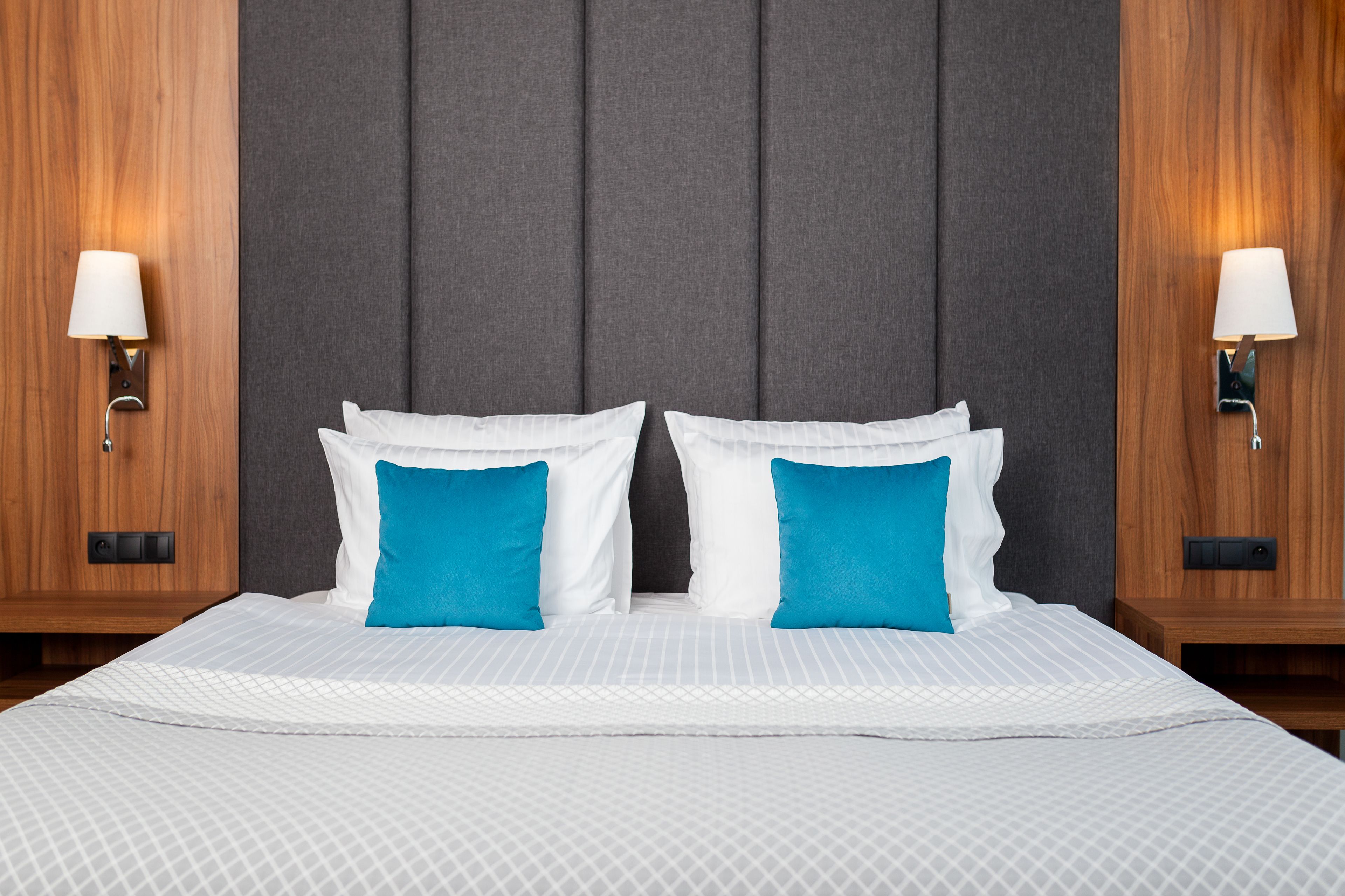A neatly made bed with white and blue pillows, flanked by two wall-mounted lamps on either side.