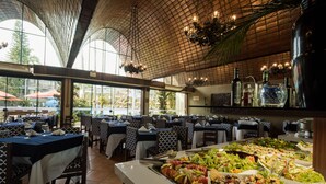 A restaurant with a buffet, tables with blue and white tablecloths, and a large window overlooking the outside. - Hotel Internacional Gravatal (Gravatal)
