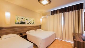 A hotel room with two beds, a painting of flowers on the wall, a desk, and a window with curtains.