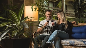 A couple sitting on a sofa with a lamp and potted plants in the background. - Hotel Internacional Gravatal (Gravatal)