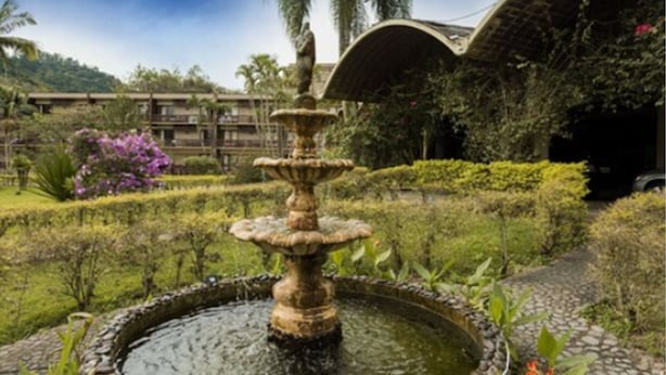 A multi-tiered stone fountain surrounded by well-maintained hedges and flowering plants, with a building in the background. - Hotel Internacional Gravatal (Gravatal)