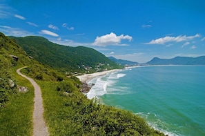 A coastal path leading to a beach with a clear view of the ocean and distant mountains.