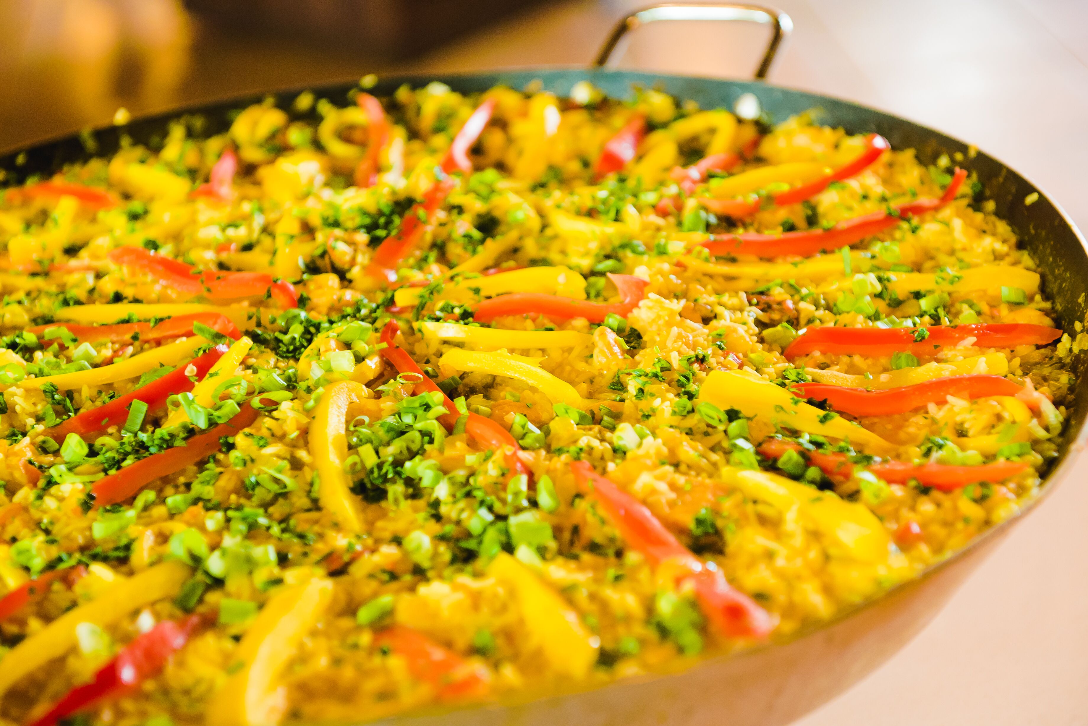 A large, oval-shaped pan filled with a colorful rice dish garnished with red and yellow bell peppers and green onions.
