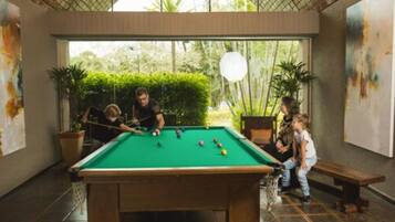 A pool table in a room with large windows, potted plants, and artwork on the walls.
