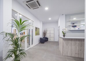 A modern reception area with a wooden reception desk, a seating area with chairs, and potted plants. - Hotel Victoria (Lloret de Mar)