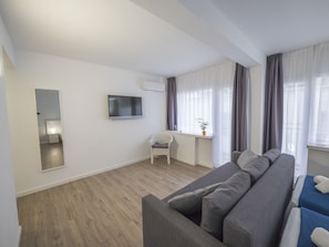 A modern living room with a grey sofa, a flat-screen TV mounted on the wall, and a small white chair. - Hotel Victoria (Lloret de Mar)