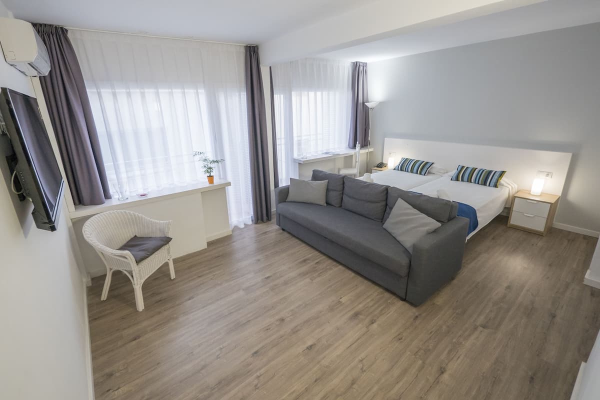 Une chambre moderne avec un canapé gris, une table de chevet blanche et un lit agrémenté d’oreillers à rayures.
