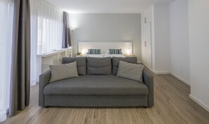 A modern living room with a grey sofa, two bedside tables with lamps, a window with curtains, and a white wardrobe. - Hotel Victoria (Lloret de Mar)