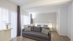 A modern living room with a grey sofa, a small table, and a bedside table with a lamp. - Hotel Victoria (Lloret de Mar)