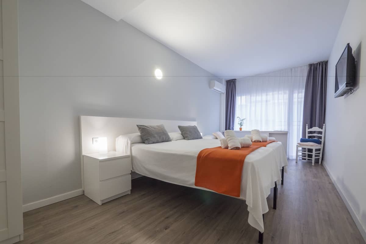 Une chambre d’hôtel moderne avec un grand lit, une table de chevet, une chaise, un téléviseur fixé au mur et une fenêtre avec des rideaux.