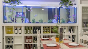 A restaurant with a long table set for dining, shelves with wine bottles, and a large aquarium above the shelves. - Hotel Victoria (Lloret de Mar)