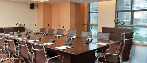 A conference room with a large table, multiple chairs, microphones, and a speaker.