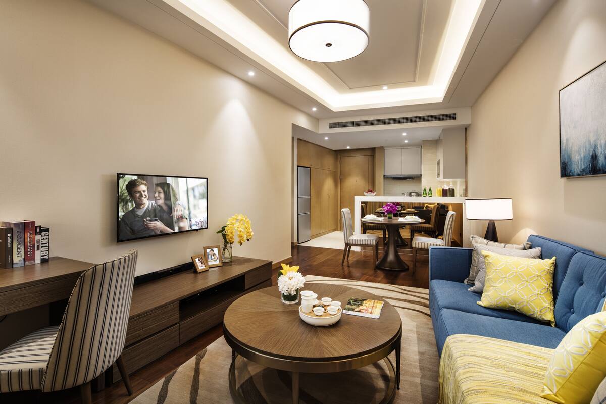 Una sala de estar moderna con televisor, comedor y cocina al fondo.