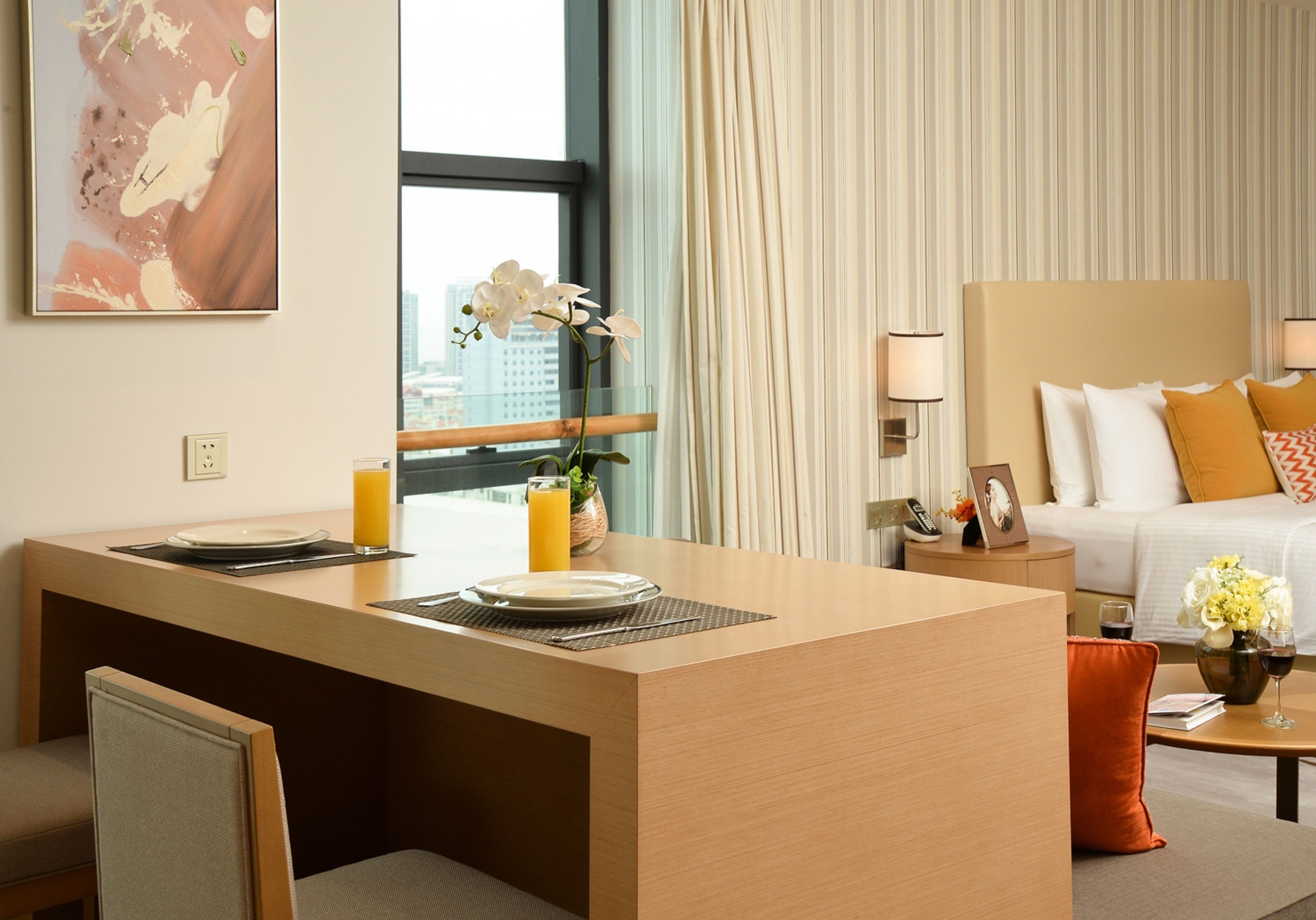 A hotel room with a dining area, a bed with a view, and a window with curtains.