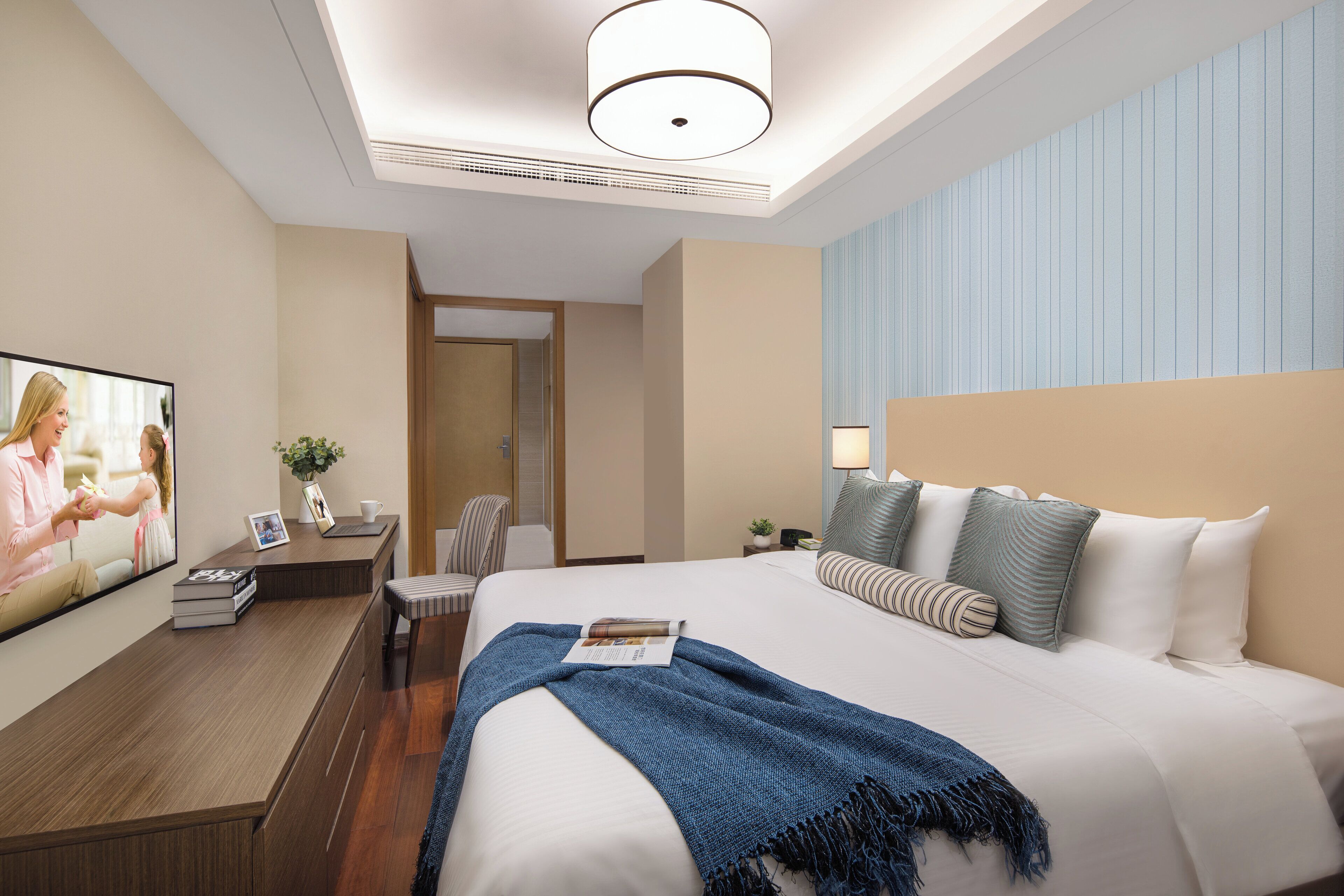A modern hotel room with a large bed, a television, a desk with a chair, and a nightstand with a lamp.