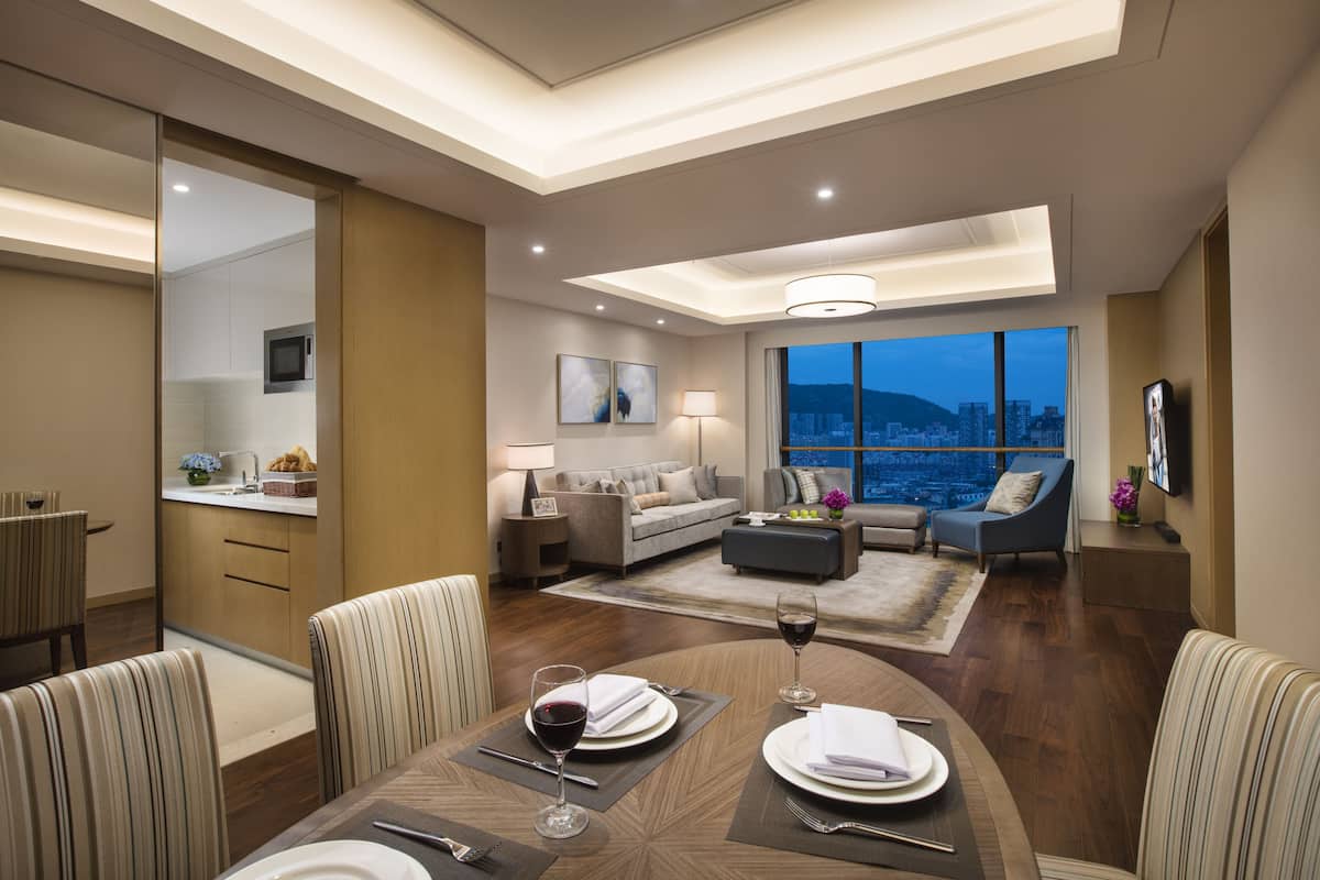 Una habitación de hotel moderna con comedor, sala de estar con vista a la ciudad y cocina.
