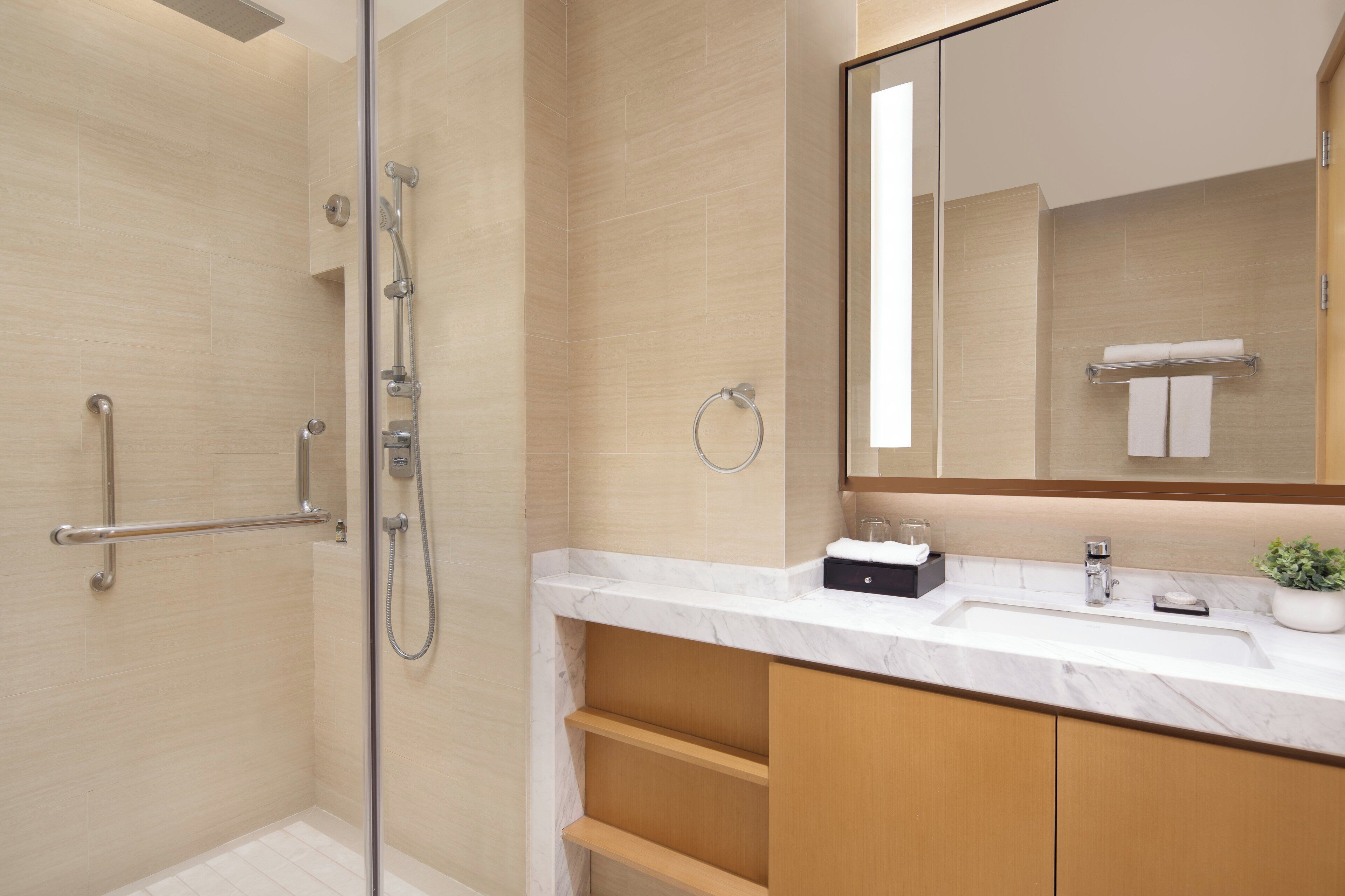 A modern bathroom with a glass-enclosed shower, a marble sink, and a large mirror.