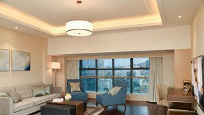 Ein modernes Wohnzimmer mit einer Couch, Sesseln, einem Couchtisch und einem Essbereich. Große Fenster bieten Blick auf die Stadt.