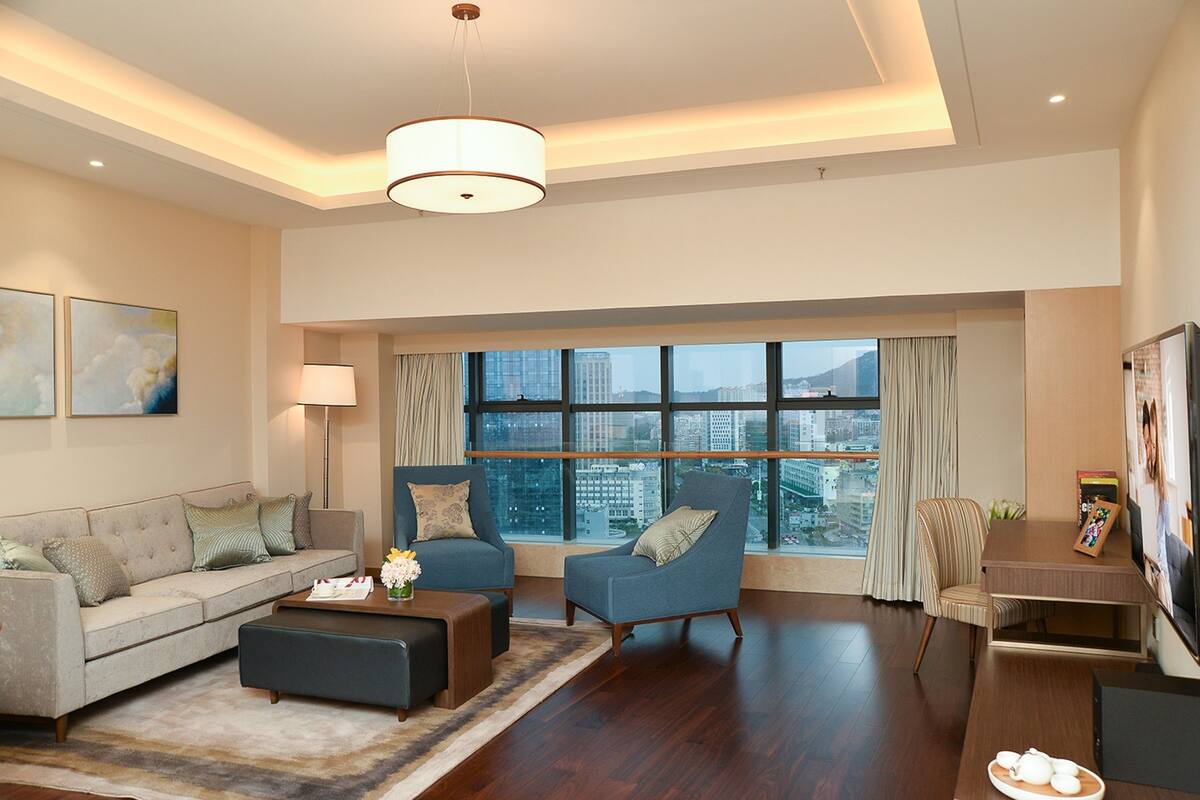 Una sala de estar moderna con sofá, sillones, una mesa de centro y una zona de comedor. Amplias ventanas ofrecen vista a la ciudad.