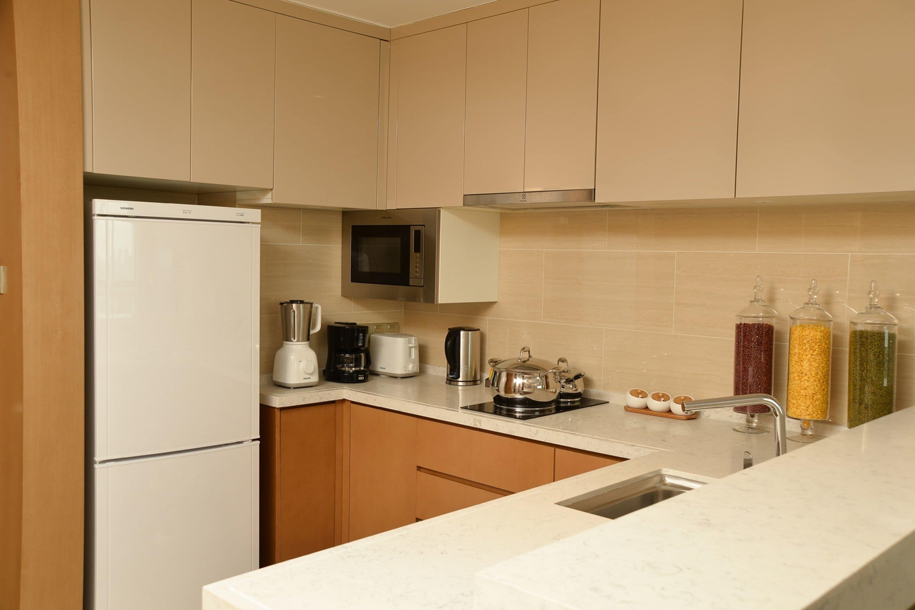 Una cocina moderna con refrigerador, microondas, cafetera, tostadora y hervidor.