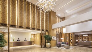 Eine geräumige Lobby mit einer Rezeption, einer Sitzecke und dekorativen Elementen wie einer großen Vase und Pendelleuchten.