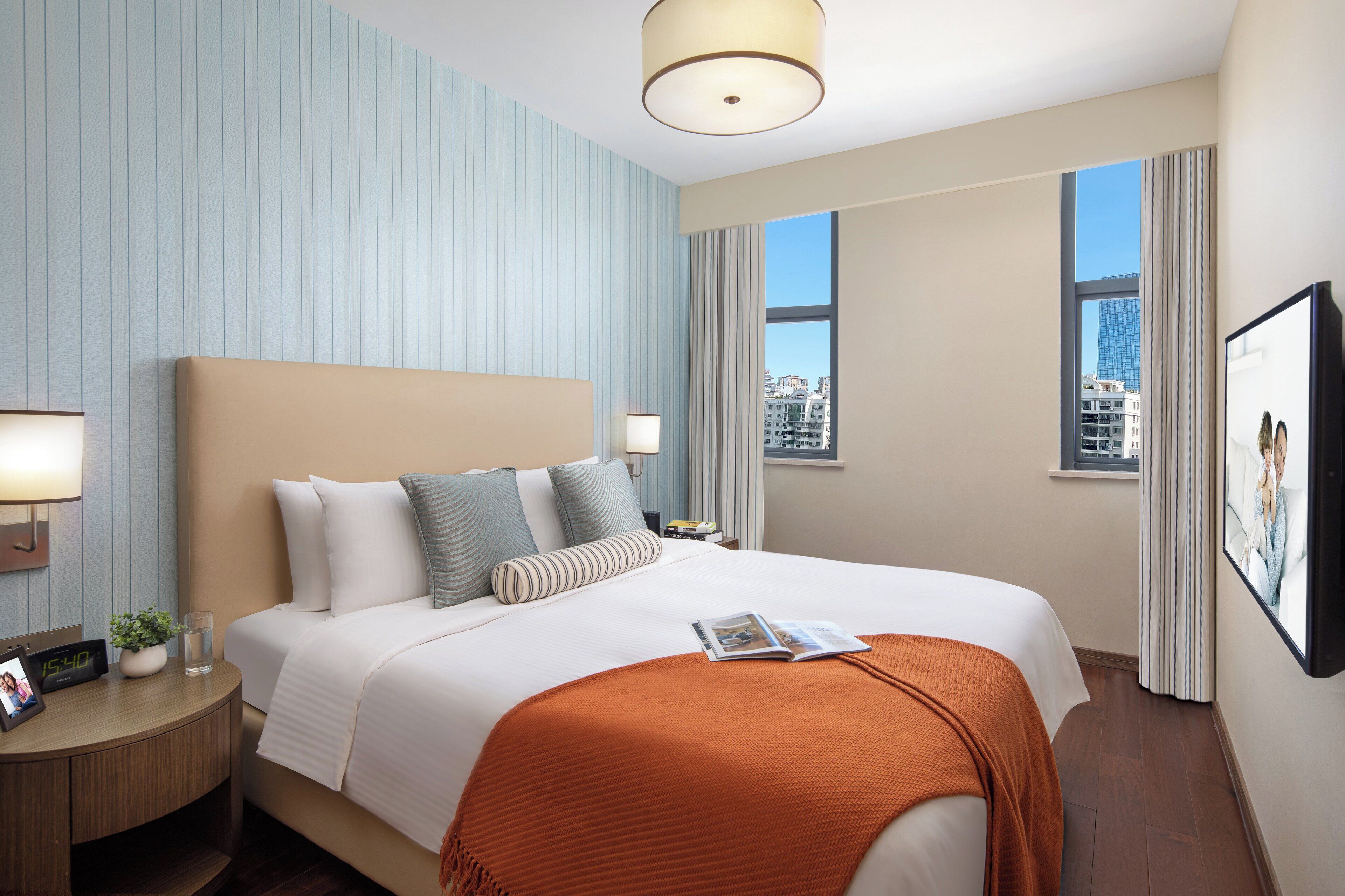 Une chambre d’hôtel avec un grand lit, une table de chevet avec une lampe, une horloge et un tableau encadré au mur.