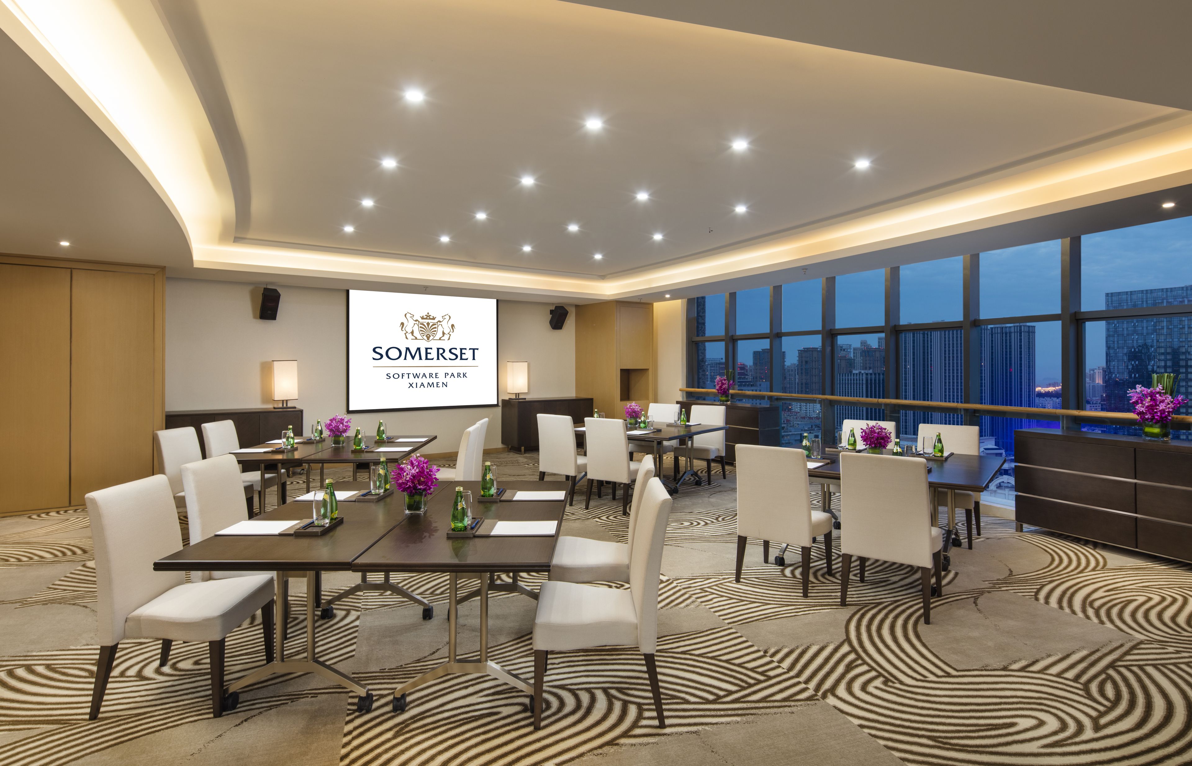 Une salle de conférence dotée d’un grand écran affichant le logo « Somerset Software Park Xi’an », de plusieurs tables avec des chaises, et offrant une vue sur la ville grâce à de grandes fenêtres.