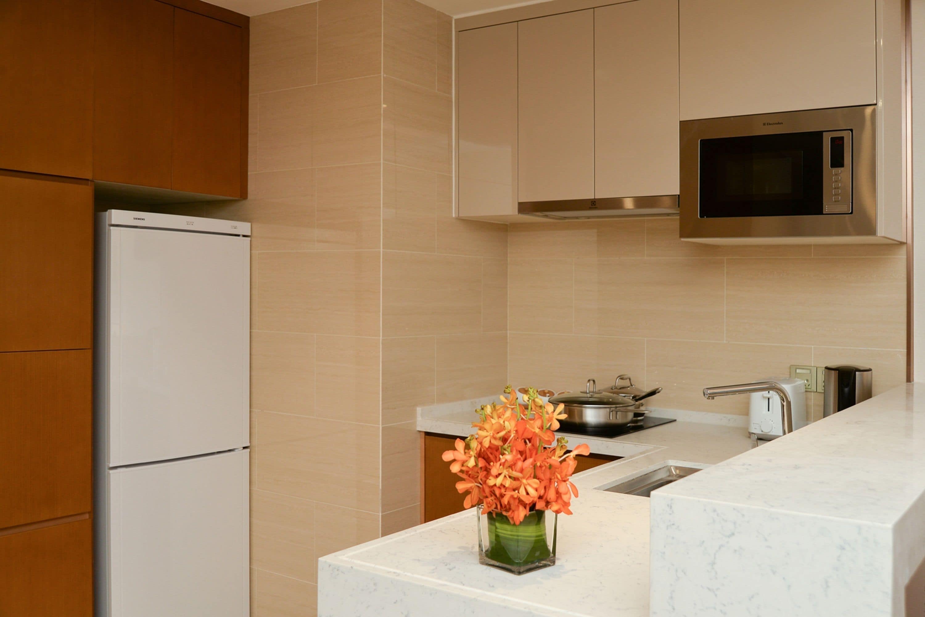 A modern kitchen with a built-in microwave, a stainless steel oven, and a white refrigerator.