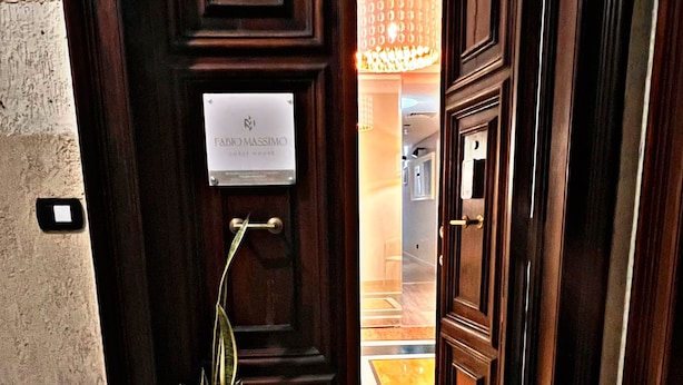 A hotel entrance with a wooden door, a potted plant, and a doormat with the hotel's name. - Fabio Massimo Guest House (Rome)