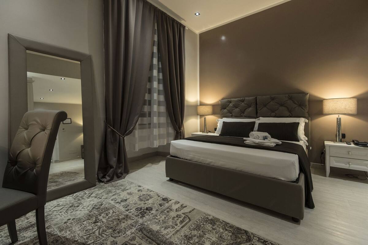 Une chambre à coucher moderne avec un grand lit, une chaise, une table de chevet et une lampe.