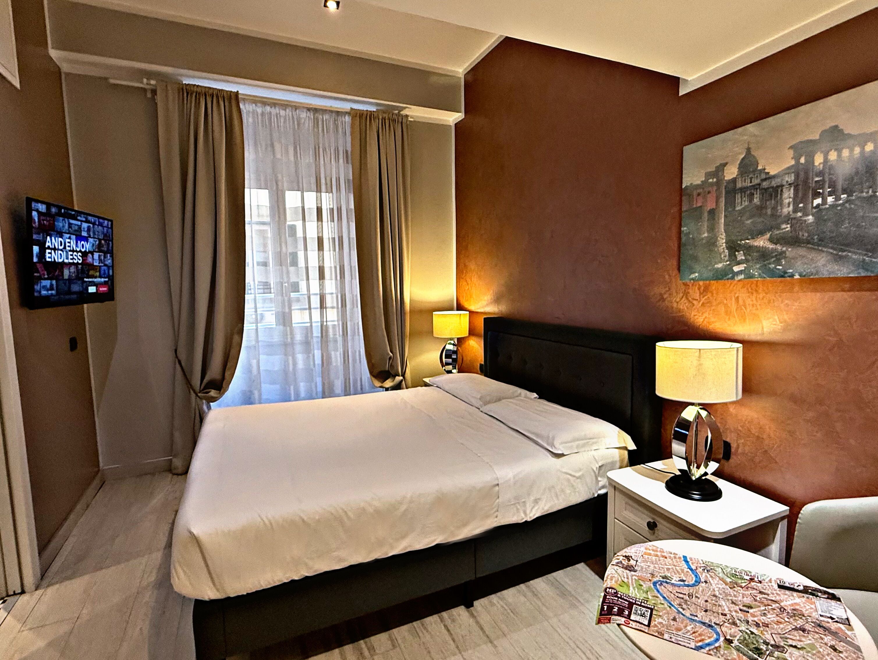 Een hotelkamer met een groot bed, een aan de muur bevestigde televisie, een kaart op het nachtkastje en een schilderij aan de wand.