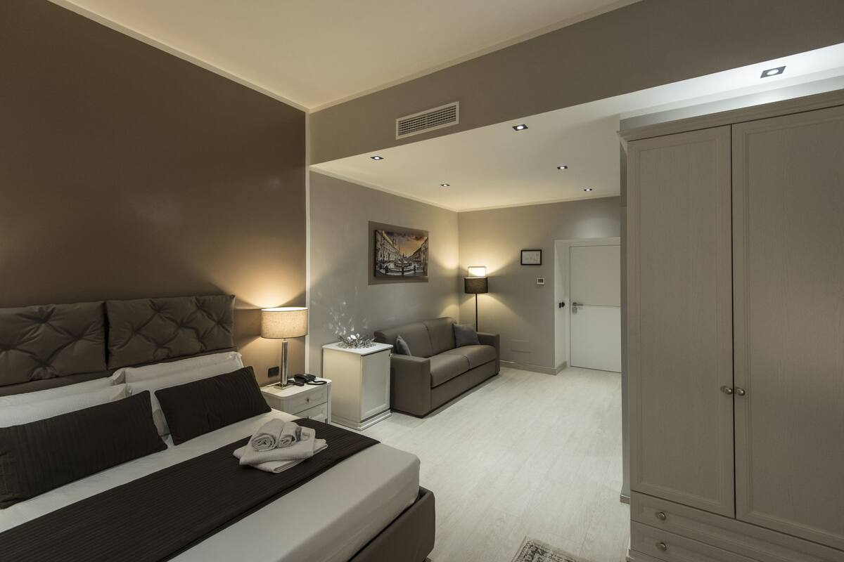Une chambre d’hôtel moderne avec un grand lit, un canapé, une armoire et un tableau au mur.