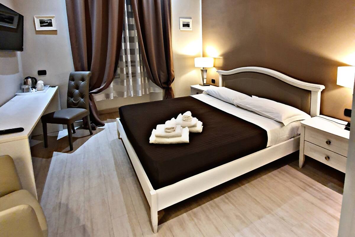 Une chambre d’hôtel avec un lit, un bureau, une chaise, une télévision et une fenêtre avec des rideaux.