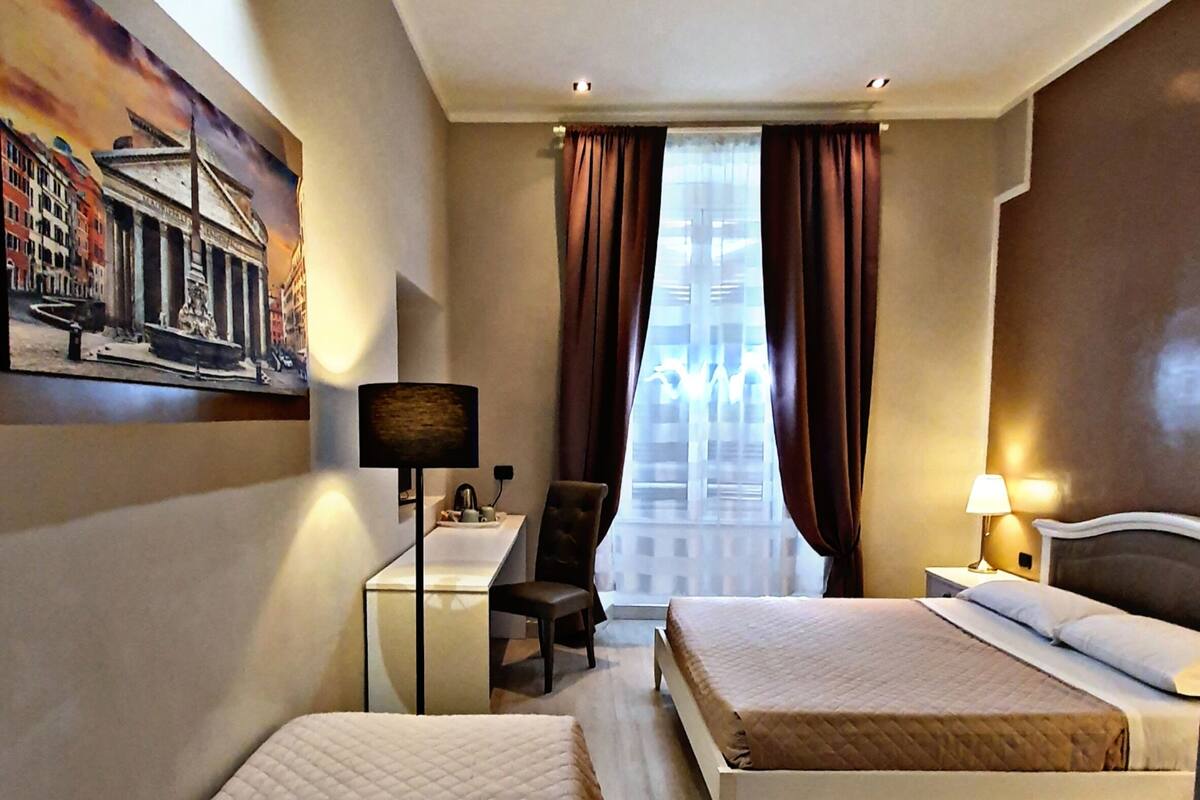 Une chambre d’hôtel avec deux lits, un bureau, une chaise, une lampe et un tableau au mur.