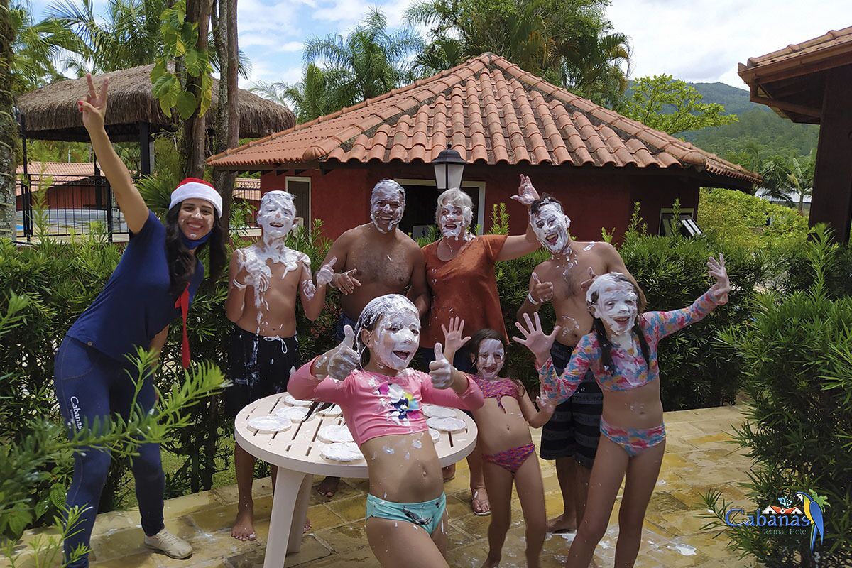 Um grupo de pessoas aproveitando uma atividade aquática ao ar livre, com um edifício de telhado de palha e vegetação exuberante ao fundo.
