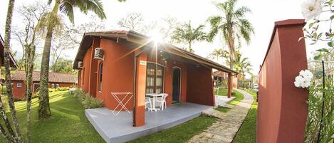 A red building with a patio, white furniture, and palm trees.