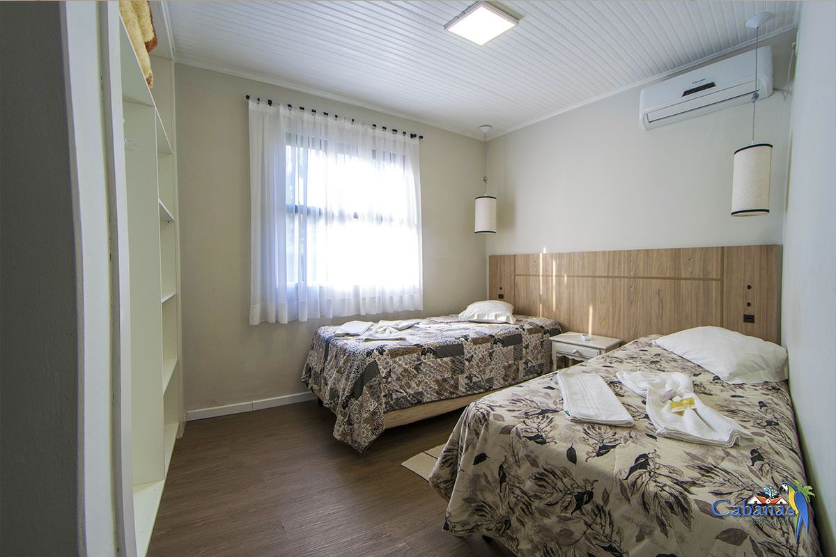 A hotel room with two beds, a window with curtains, a ceiling fan, an air conditioning unit, and a wooden headboard.